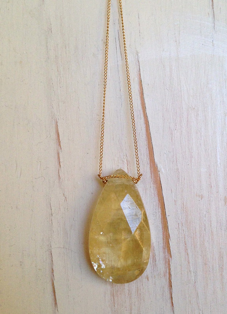 May include: A gold chain necklace with a large, teardrop-shaped, faceted, yellow citrine pendant.