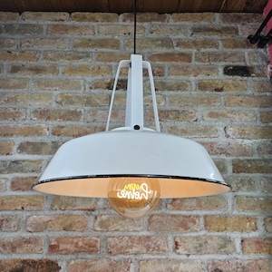 May include: White pendant light fixture with a black rim and a clear light bulb. The light fixture is hanging from a brick wall.