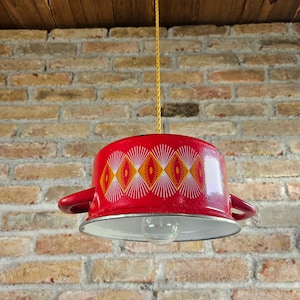 May include: A red and white patterned metal lampshade with a light bulb hanging from a ceiling. The lampshade has a geometric design with yellow accents.
