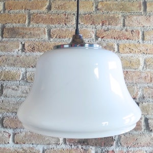 May include: A white, bell-shaped pendant light fixture with a chrome-colored trim. The light hangs from a black cord against a brick wall background. The fixture has a smooth, glossy finish and a classic design.