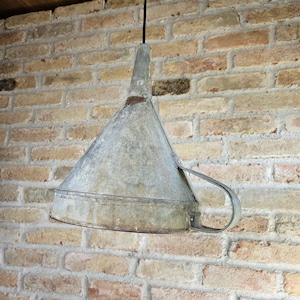 May include: A vintage-style metal funnel pendant light. The light fixture is suspended from a black cord against a brick wall. The funnel has a handle and a weathered, galvanized finish, adding a rustic charm.