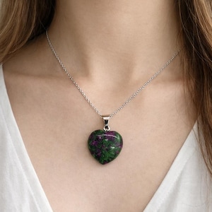 Könnte beinhalten: Eine silberne Halskette mit einem herzförmigen Anhänger. Der Anhänger ist eine Mischung aus grünen und roten Farben. Die Halskette wird um den Hals getragen.