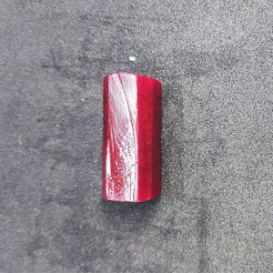 May include: A rectangular, red wooden object with a glossy finish. The object has a slightly rounded top and visible wood grain. The item is set against a dark grey, textured background.
