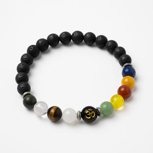 Op de afbeelding: Een kralenarmband met zwarte lavasteen kralen en kleurrijke chakra kralen. De armband bevat kralen in blauw, geel, rood, groen en wit, met een zwarte kraal met een gouden Om-symbool.