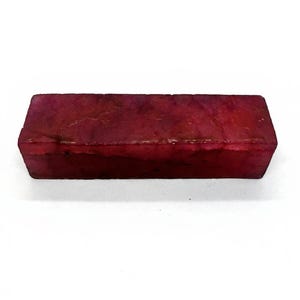 Może przedstawiać: Prostokątny blok z głębokiego czerwonego materiału. Blok ma lekko teksturowaną powierzchnię, prawdopodobnie kamień szlachetny lub minerał. Kolor to bogaty, ciemnoczerwony z odcieniami.