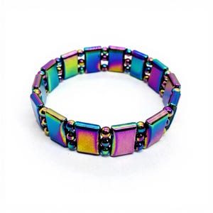 May include: An iridescent magnetic bracelet. The bracelet is made up of rectangular and round beads that shift in colour from blue to purple, green, and gold. The bracelet is designed to be worn on the wrist.