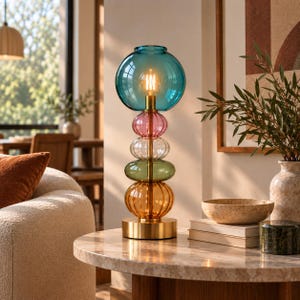 May include: A table lamp featuring a stack of five colourful glass spheres in teal, pink, clear, green, and amber, supported by a central brass rod and a circular brass base. The lamp includes an exposed filament bulb inside the top teal sphere.