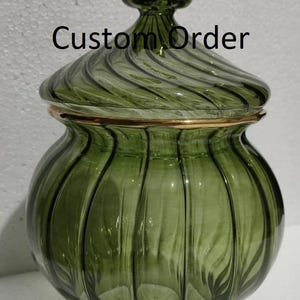May include: A green glass jar with a lid, featuring a gold rim and a decorative finial. The jar has a ribbed design and the text "Custom Order" is visible on the front.