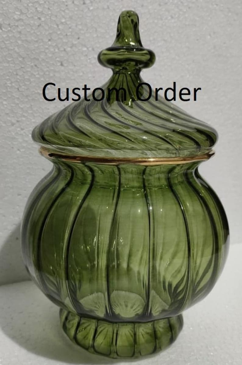 May include: A green glass jar with a lid, featuring a gold rim and a decorative finial. The jar has a ribbed design and the text "Custom Order" is visible on the front.