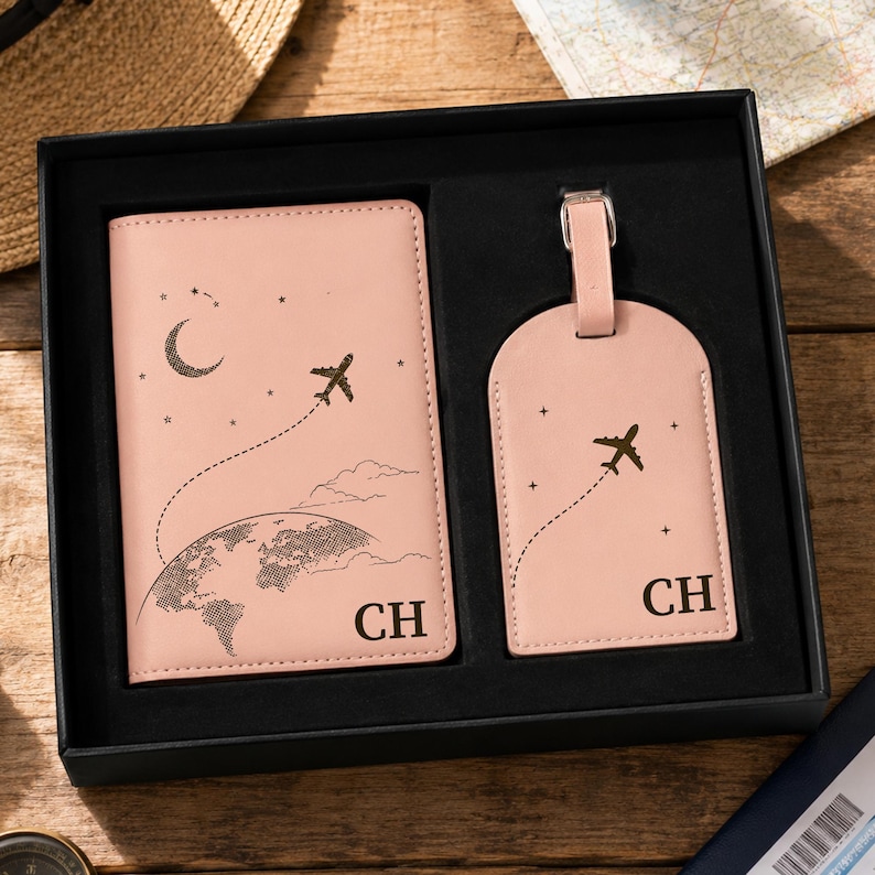 A beautifully presented blush pink personalized travel set displayed inside a luxury black gift box. The set includes a matching passport holder and luggage tag, both featuring a minimalist travel-themed design with an airplane flight path, stars, a crescent moon, and a world map. The bottom corner is customized with initials “CH,” showing elegant personalization. The packaging gives a premium gift-ready feel, perfect for travel lovers.
