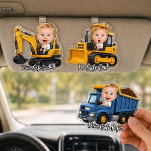 Peut inclure: Trois ornements de pare-soleil de voiture en acrylique transparent représentant des engins de chantier avec le visage d'un bébé au volant. Une pelleteuse avec Drive Safe DadAy, un bulldozer avec Be Safe Dad et un camion benne bleu avec Drive Safe Papa.