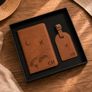 May include: A tan passport holder and a matching luggage tag set inside a black box. Both items feature a laser-engraved design of an airplane, a crescent moon, stars, and a globe, along with the initials CH embossed on the bottom right corner.