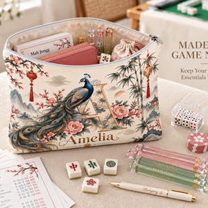 May include: A cream-coloured zippered pouch featuring a peacock, floral motifs, and the letter A with the name Amelia. The pouch contains pens and a small pouch. Text reads: MADE FOR GAME NIGHT, Keep Your Mahjong Essentials Together, and Mah Jongg.