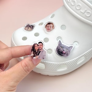 Può includere: Uno zoccolo in schiuma bianca con quattro ciondoli in acrilico personalizzati fissati nei fori di ventilazione. I ciondoli mostrano fotografie stampate di un cagnolino, un bambino, una coppia e un gatto grigio con la lingua di fuori.