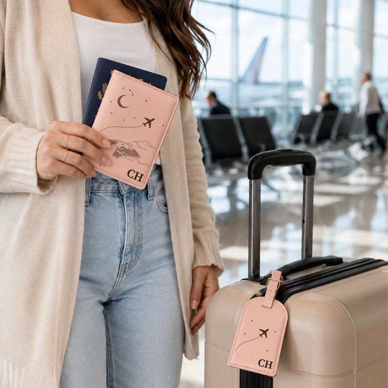 May include: A light pink passport holder and a matching luggage tag, both featuring a dark brown graphic of a crescent moon, stars, and an airplane with a flight path. Each item is personalized with the black embossed initials CH.