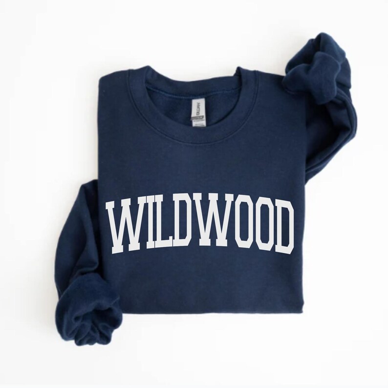 May include: A navy blue sweatshirt with the word "WILDWOOD" printed in large, white, block letters across the chest. The sweatshirt has a crew neck and long sleeves. The garment is displayed on a white background.