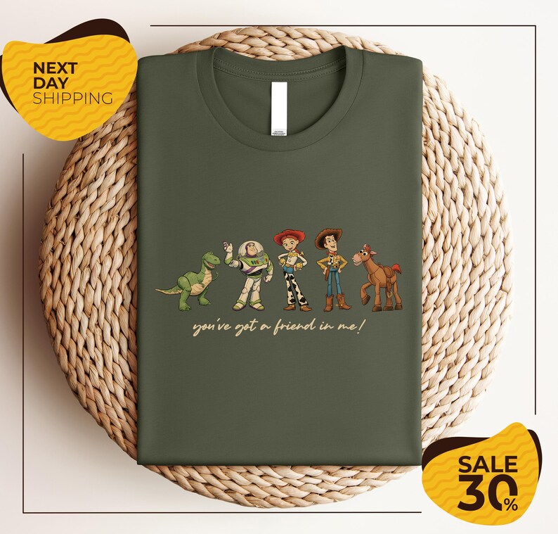 A green t-shirt with a graphic design featuring characters from the Toy Story movie, including Woody, Buzz Lightyear, and a dinosaur. The text below the characters reads "you've got a friend in me!"