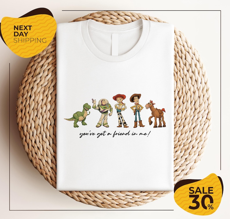 A white t-shirt with a graphic design featuring characters from the Toy Story movie, including Woody, Buzz Lightyear, and a horse. The text below the characters says "you've got a friend in me!"
