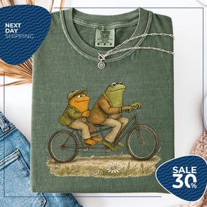 a green t-shirt with a cartoon illustration of two frogs riding a bicycle, accompanied by a price tag of $30.