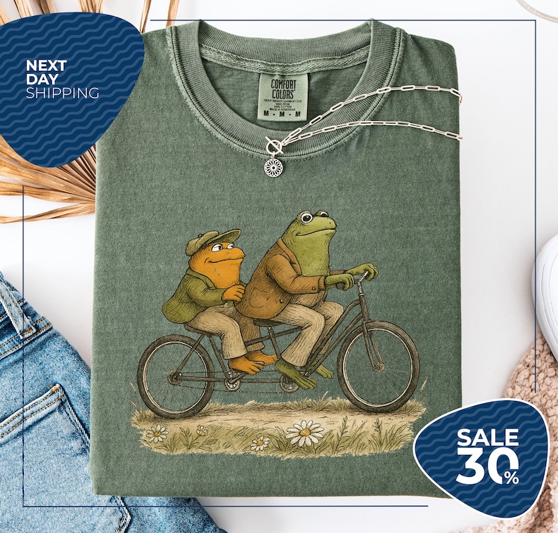 a green t-shirt with a cartoon illustration of two frogs riding a bicycle, accompanied by a price tag of $30.