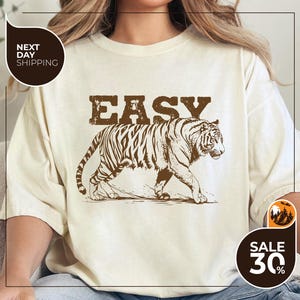 A person wearing a white t-shirt with a graphic of a tiger and the word "EASY" printed on it.