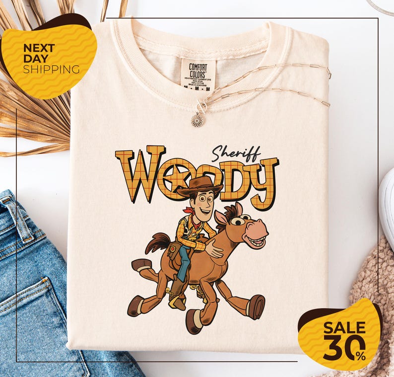 a white t-shirt with a cartoon image of Woody, a character from the Toy Story movie, riding a brown horse. The t-shirt is displayed on a white background, and there are yellow and black sale signs indicating a 30% discount.