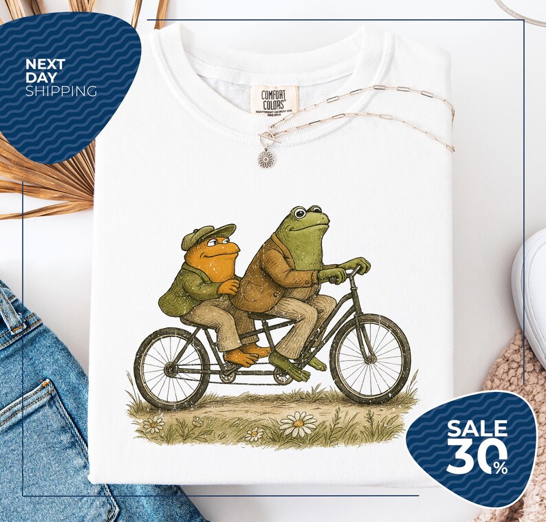 a white t-shirt with a drawing of two frogs riding a bicycle, accompanied by a sale sign indicating a 30% discount.