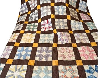 May include: A handmade quilt with a star pattern. The quilt features a grid of dark brown squares with yellow corner accents. Each square contains a star design in various pastel colors, including blue, pink, and white. The quilt is a traditional style.