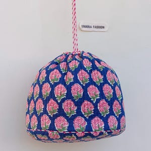 May include: A blue fabric drawstring bag with a pink floral pattern. The bag is suspended by a red and white striped cord. The text "UMARIA FASHION" is on a white label.