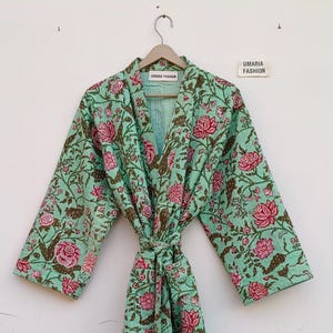 Könnte beinhalten: Minzgrüner Bademantel mit floralem Muster mit rosa Blüten und braunen Blättern. Der Bademantel ist an der Taille gebunden und hängt an einem Holzbügel. Der Text "UMARIA FASHION" ist auf einem Etikett zu sehen.