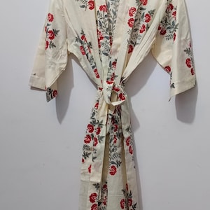 May include: Cream-colored floral print robe with red roses and green leaves. The robe has a tie closure and wide sleeves. The text "UMARIA FASHION" is visible on a tag. This robe is perfect for lounging.