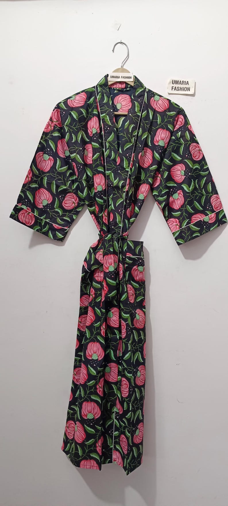 May include: A black floral print robe with pink flowers and green leaves. The robe has white trim and a tie closure. The text "UMARIA FASHION" is visible on the hanger and a tag.