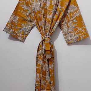 May include: Mustard yellow robe with a floral pattern in white and gray. The robe has wide sleeves, a tie belt, and white trim. The text "UMARIA FASHION" is visible on a tag and the hanger.