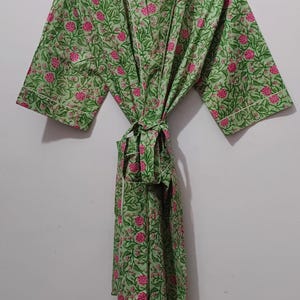 May include: A green floral print robe with pink flowers and white trim, hanging on a wooden hanger. The robe is tied at the waist. The brand name "UMARIA FASHION" is visible on the hanger and a tag.