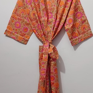 May include: A floral print robe in shades of orange, pink, and tan, hanging on a white wall. The robe features a tie closure and white trim. The brand name "UMARIA FASHION" is visible on the hanger.