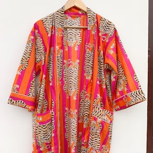 May include: An open-front robe with a vibrant tiger stripe pattern in orange, pink, and black. The robe features a striped design with tiger illustrations, pockets, and white trim. The robe is hanging on a wooden hanger.