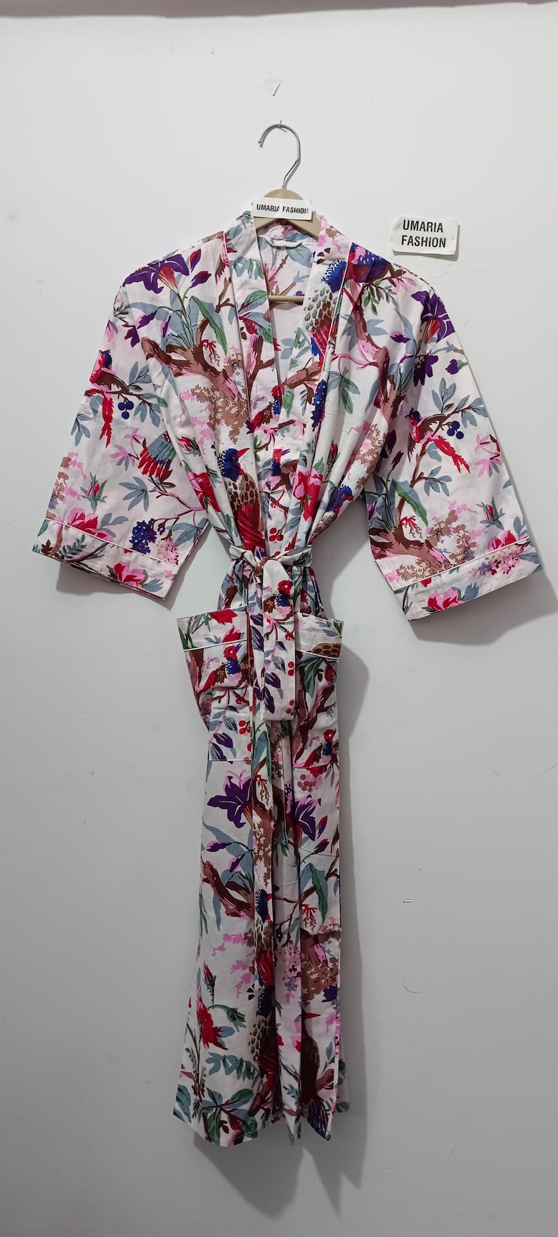 May include: White floral print robe with a tie belt. The robe features a colorful bird and floral pattern in shades of red, pink, purple, and green. The text "UMARIA FASHION" is visible on a tag.