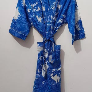 May include: Blue and white patterned robe with a palm tree design. The robe is hanging on a hanger and tied at the waist. The text "UMARIA FASHION" is visible on the hanger and a tag.