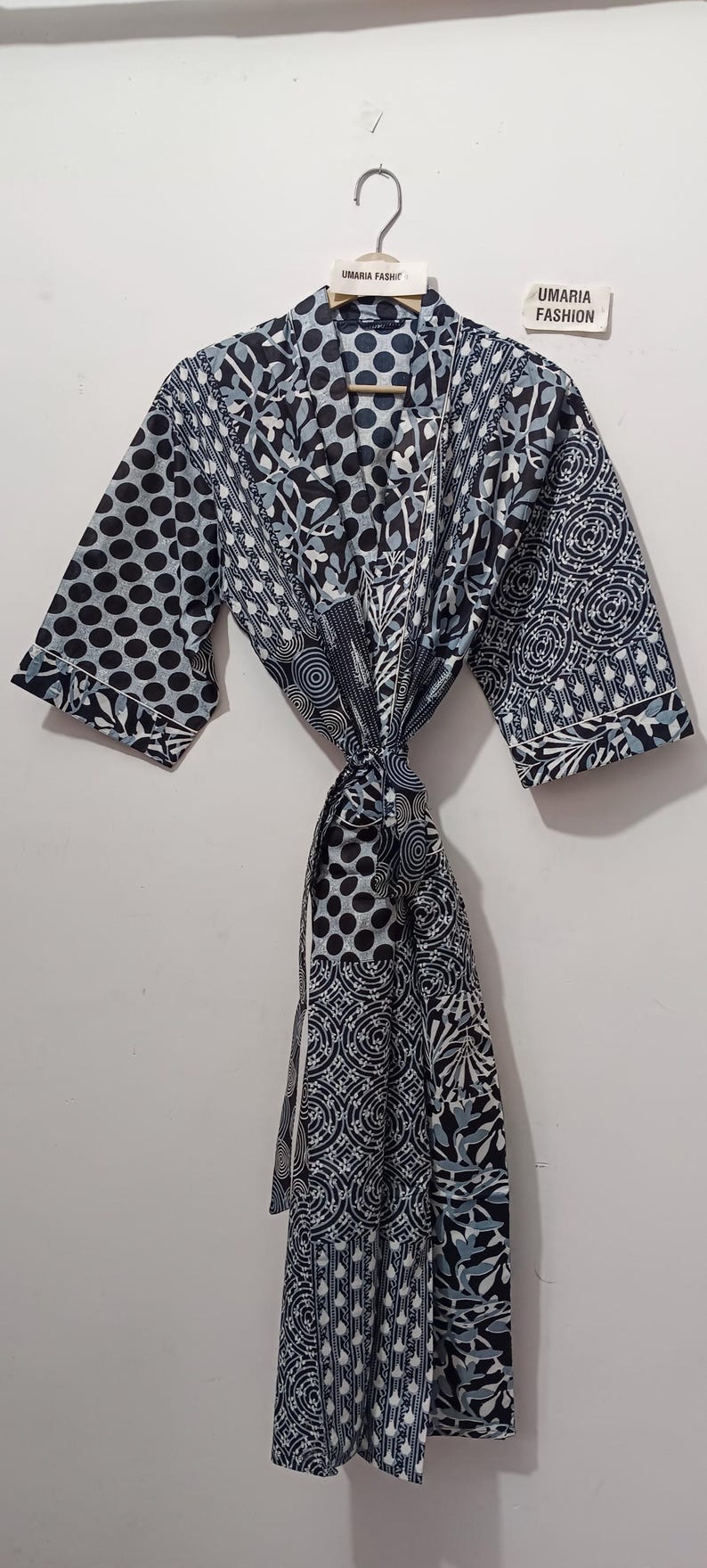 May include: A patterned robe with a tie closure. The robe features a mix of black, white, and light blue patterns, including polka dots, floral designs, and geometric shapes. The label reads "UMARIA FASHION".