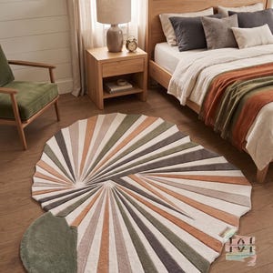 May include: A large, irregularly shaped area rug featuring a sunburst pattern with alternating rays in shades of sage green, terracotta, cream, and charcoal gray. The rug has a textured pile and includes a small rectangular tag with text.
