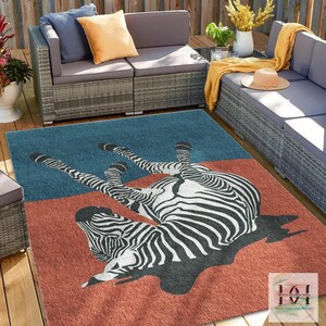 Op de afbeelding: Een rechthoekig buitenkleed met een zebra-ontwerp. Het kleed heeft een tweekleurig kleurenschema met een blauwe bovenkant en een roestkleurige onderkant. De zebra is afgebeeld in zwart en wit.