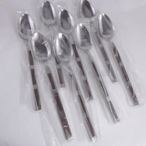 Puede incluir: Un juego de ocho cucharas de acero inoxidable, cada una envuelta individualmente en plástico transparente. Las cucharas tienen un cuenco ovalado pulido y un mango con un centro de madera marrón oscuro y detalles plateados. Las cucharas son para comer.