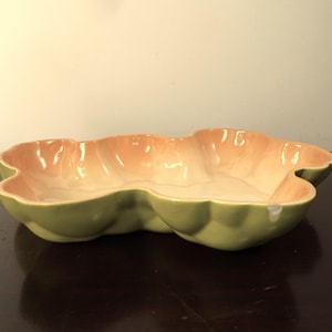 May include: A ceramic serving dish with an unusual, organic shape. The dish has a light green exterior and a peach-coloured interior. The dish has a glossy finish and is likely used for serving food or as a decorative piece.