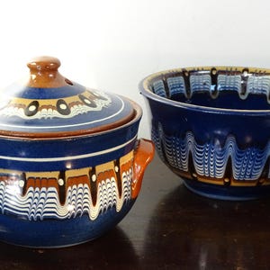 Peut inclure: Deux bols en céramique avec un motif ondulé bleu et blanc. L'un des bols a un couvercle et des poignées, l'autre est ouvert. Les bols ont des accents marron et jaune. Les bols sont probablement destinés à servir des aliments.