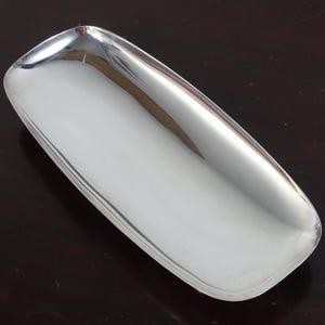 May include: A rectangular silver-colored tray with rounded corners and a smooth, reflective metallic surface. The tray features slightly raised edges and a shallow, elongated basin, presenting a clean, polished appearance with no additional patterns.