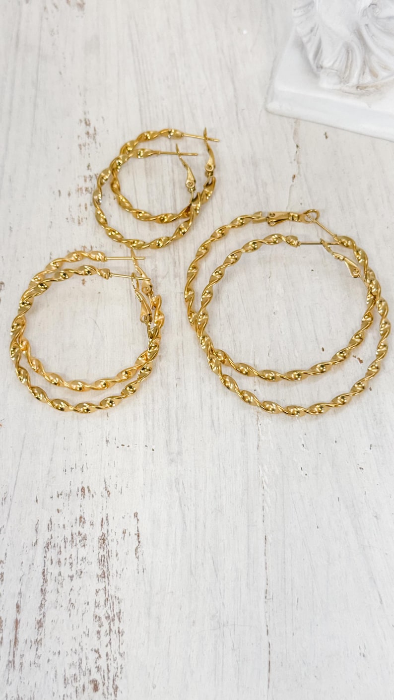 May include: Three pairs of gold-toned hoop earrings, each featuring a twisted rope-like texture. The earrings are arranged in varying sizes, with each pair consisting of two circular hoops connected by a hinged post closure mechanism.