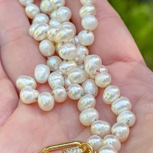 May include: A white pearl necklace with a gold clasp featuring a small row of clear rhinestones. The necklace is strung on a thin white thread.