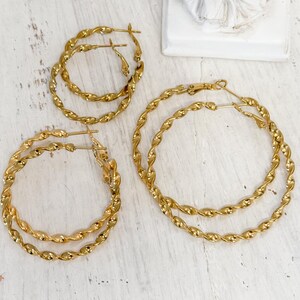 May include: Four gold-toned hoop earrings with a twisted rope texture. The set includes two smaller hoops and two larger hoops, each featuring a thin post closure. The earrings have a polished, reflective metallic finish and a circular shape.