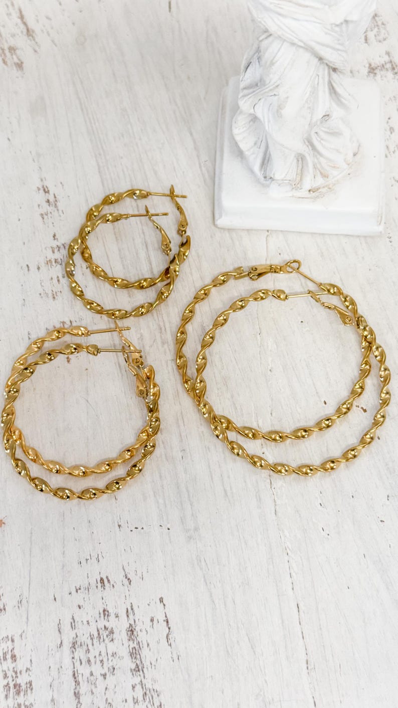 May include: Four gold-toned hoop earrings with a twisted rope texture. The set includes two smaller hoops and two larger hoops, each featuring a thin post closure. The earrings have a polished, reflective metallic finish and a circular shape.