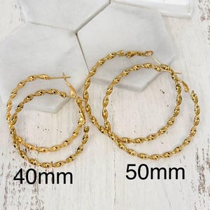 May include: Two pairs of gold-toned hoop earrings with a twisted rope texture. One pair is labelled 40mm and the other pair is labelled 50mm. The earrings feature a circular design with a hinged post closure, showcasing a polished metallic finish.